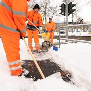 Arbeiter streuen Straße und fegen Schnee
