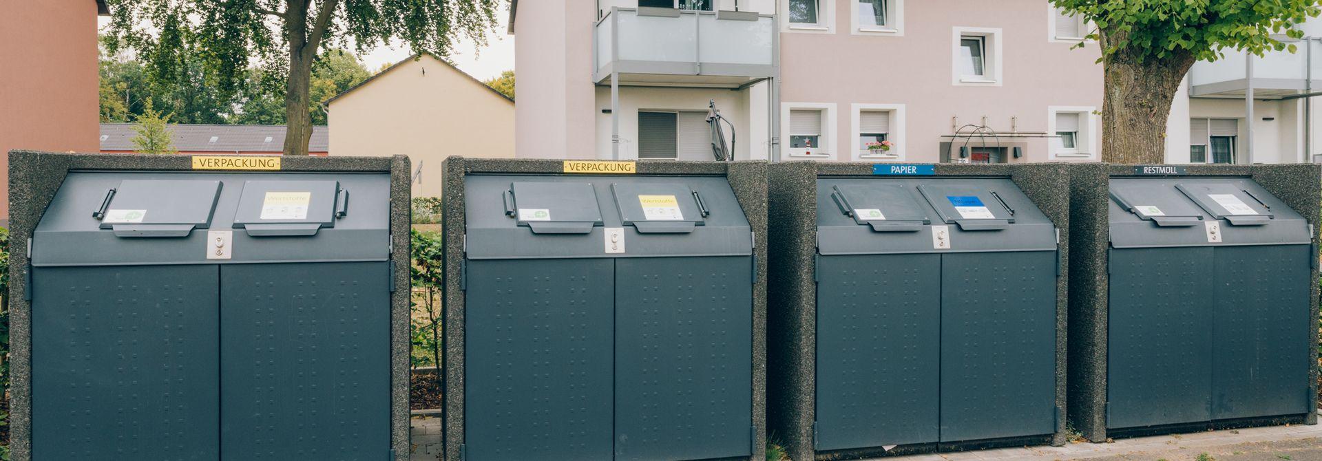 Behälter mehrerer Abfallfraktionen stehen nebeneinander vor einem Wohnhaus