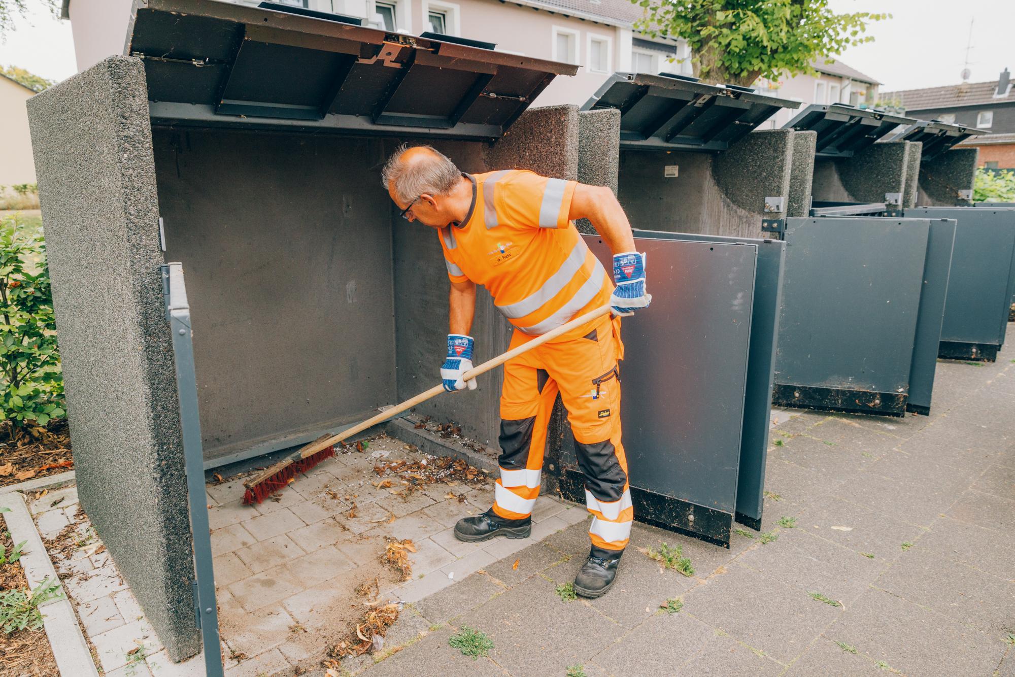 Mitarbeiter reinigt einen Behälterstandplatz mit einem Besten