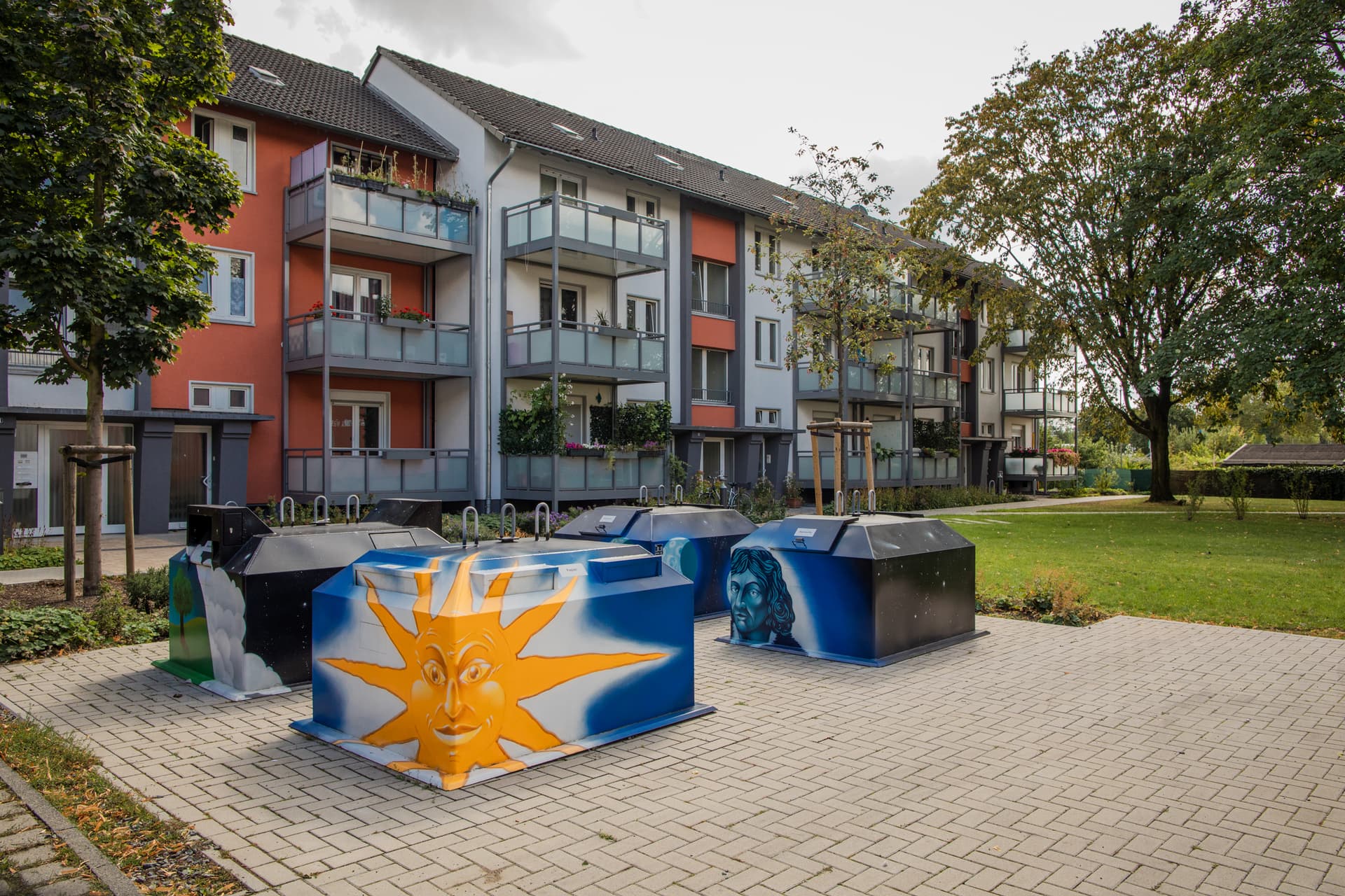 Vier Halbunterflurbehälter mit individueller Lackierung vor einem Wohnhaus