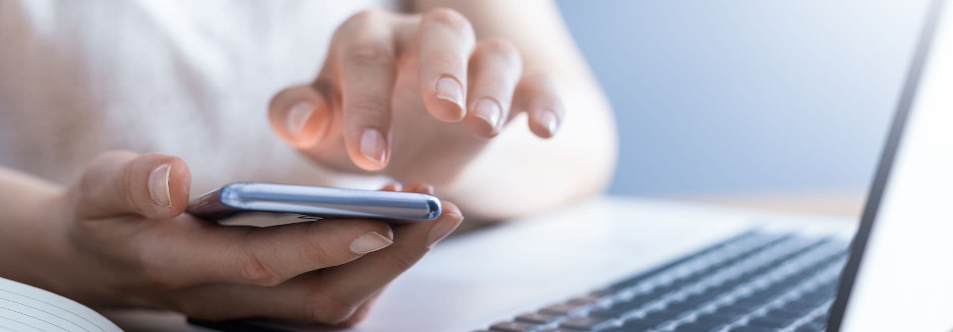 Frau hält Smartphone in der Hand, davor liegen ein Notebook und ein Heft