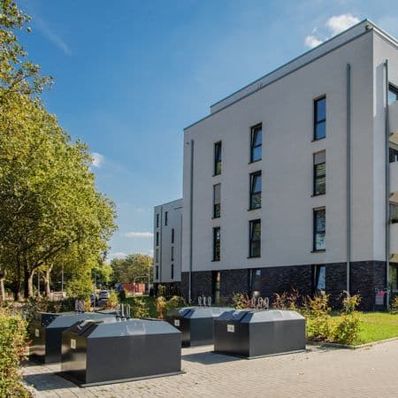 Vier graue Halbunterflurbehälter vor weißem Mehrfamilienhaus