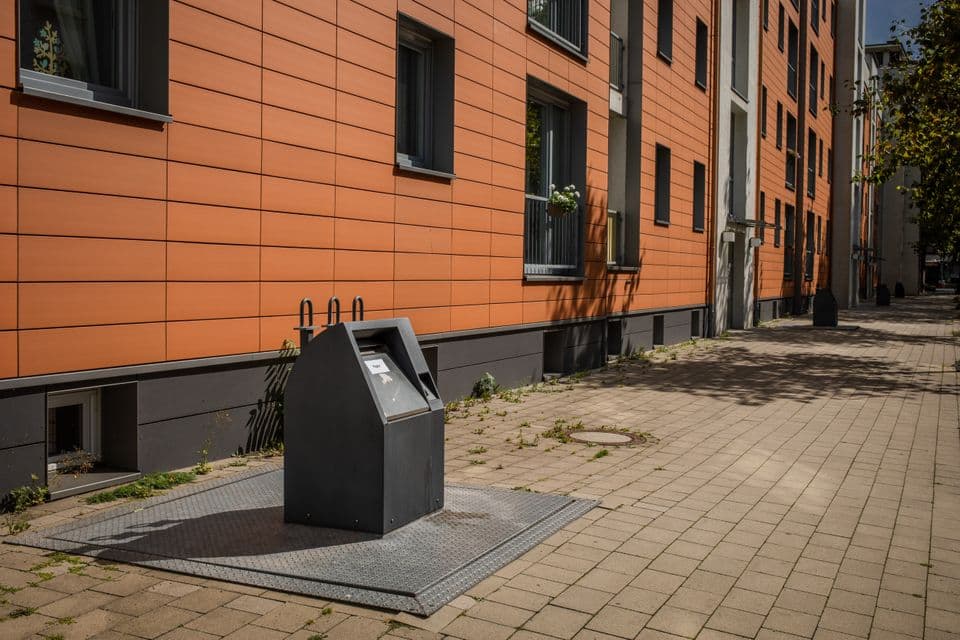 Ein grauer Vollunterflurbehälter vor einem Wohnhaus