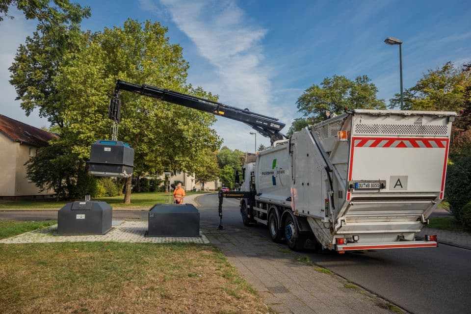Ein Müllwerker leert mit Hilfe eines Krans einen einen Halbunterflurbehälter