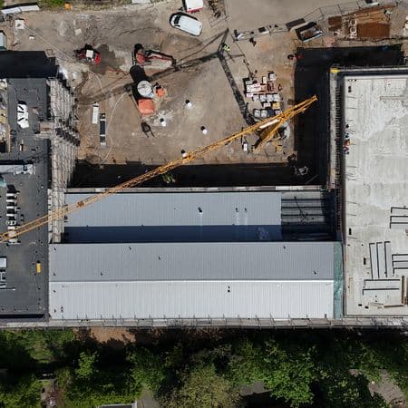 Luftaufnahme einer Baustelle mit zwei rechteckigen Gebäuden, Baukran und Maschinen