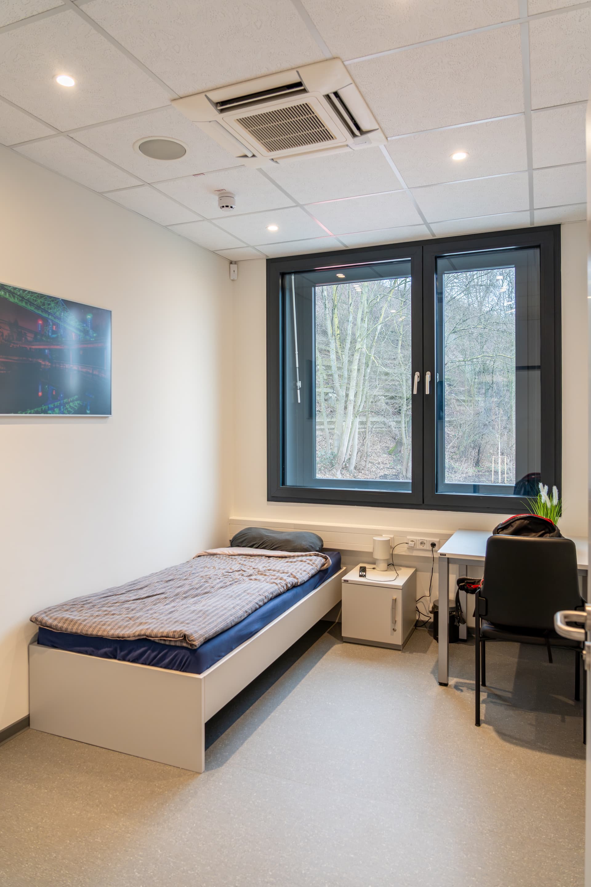 Ruheraum mit einem Bett vor dem Fenster und daneben einem Tisch mit Stuhl