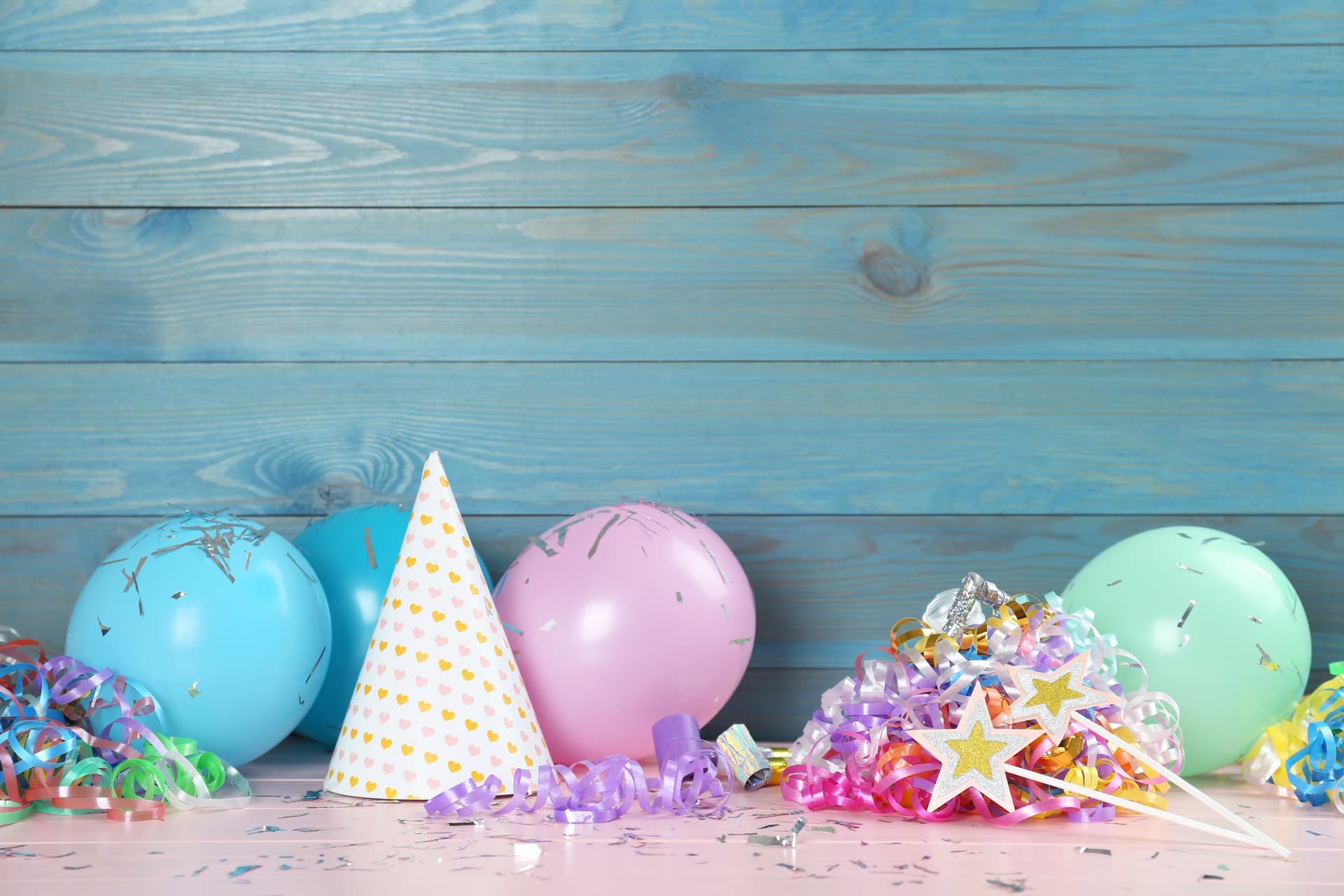 Luftballons und weitere Karnevalsdeko liegen auf einer Fläche , dahinter ist eine hellblaue Holzwand.